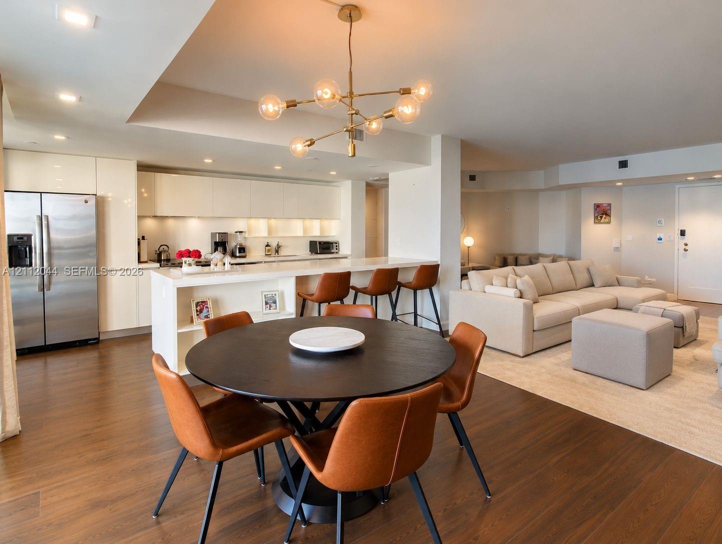 Open-concept kitchen featuring high-gloss cabinetry, stainless steel refrigerator, breakfast bar with waterfall-edge countertop, recessed lighting, an