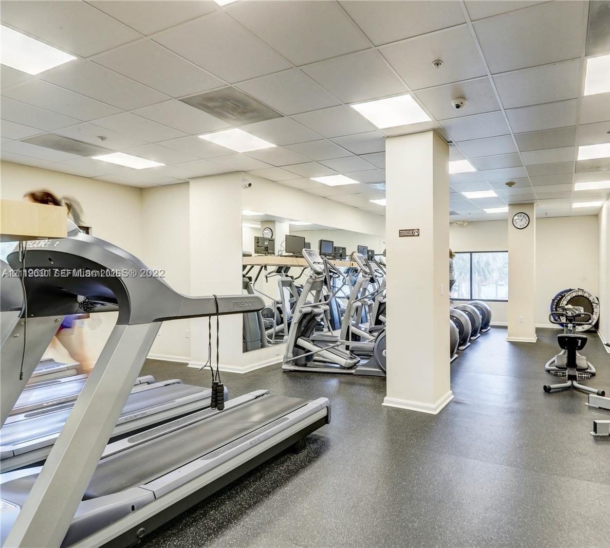 Fitness center featuring grid ceiling lighting, wall-to-wall mirrors, and resilient rubberized flooring