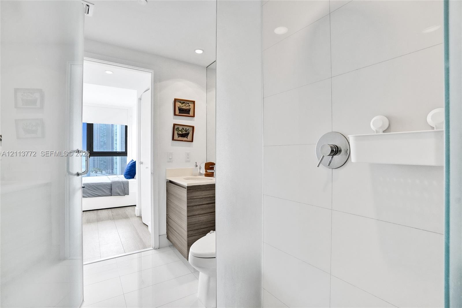 Full-height white tile shower enclosure featuring polished chrome fixtures, glass door, wood-finish cabinetry, and solid surface countertop