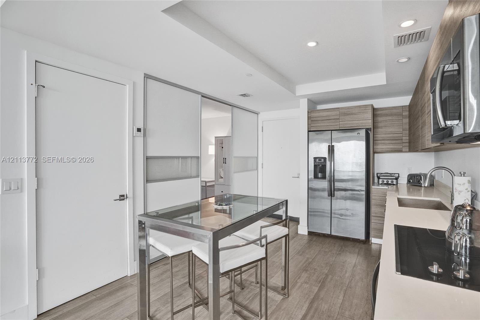 Kitchen featuring horizontal wood-grain cabinetry, stainless steel side-by-side refrigerator, recessed lighting, wood-finish flooring, and solid-surfa