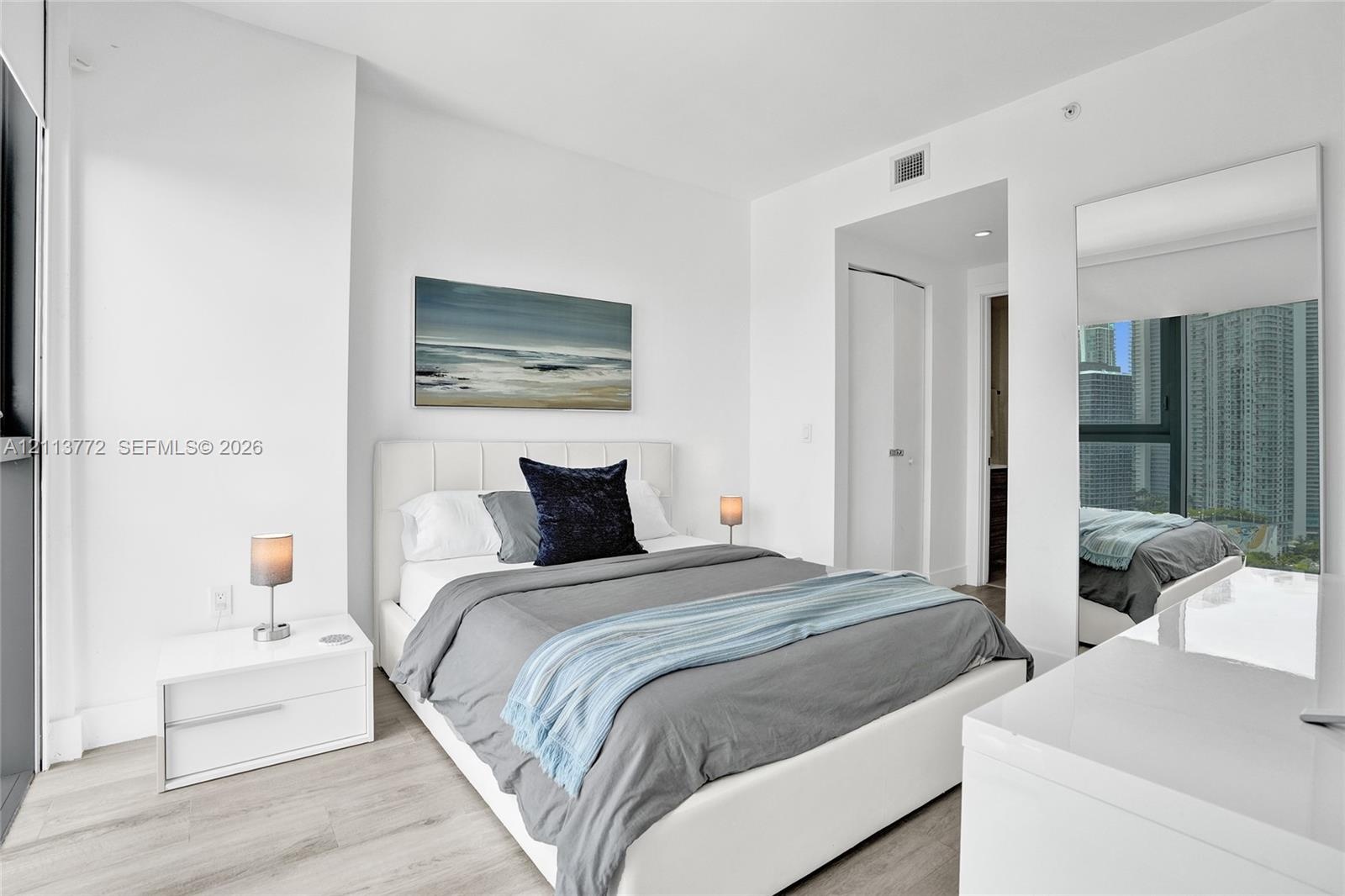 Neutral-toned wood-finish flooring, floor-to-ceiling window, and full-length wall mirror