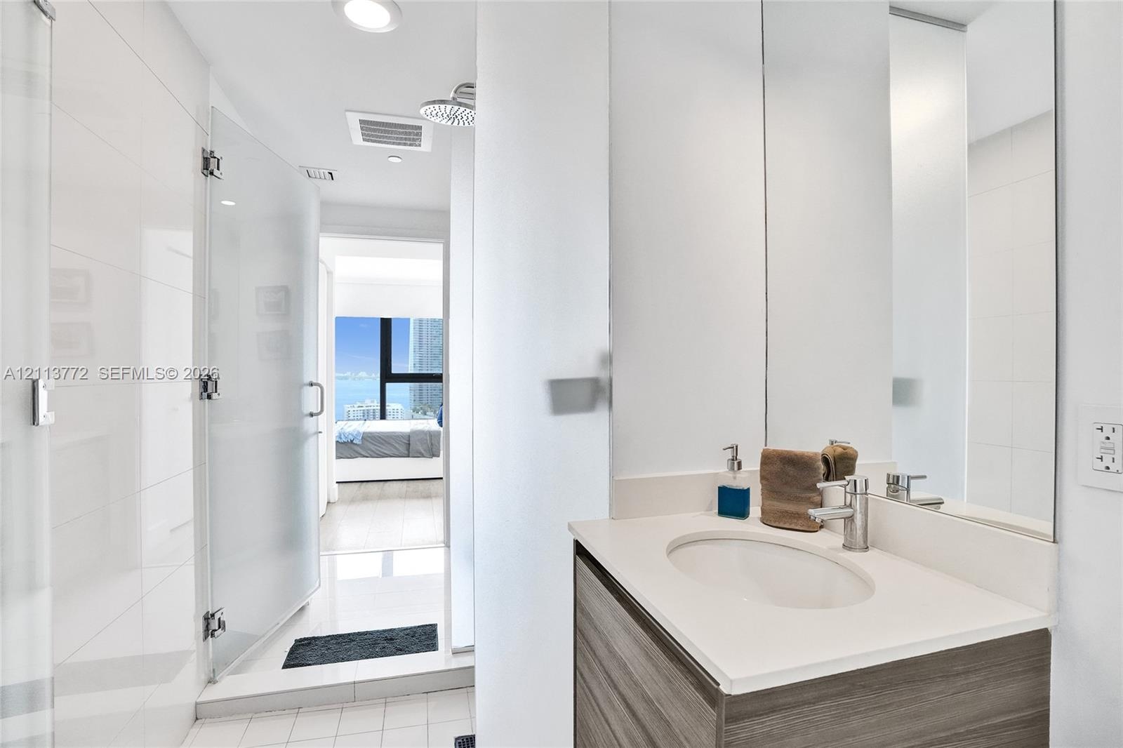 Bathroom featuring a wood-finish vanity with a light-toned countertop, integrated sink, chrome faucet, glass-enclosed shower, and full-height wall mir