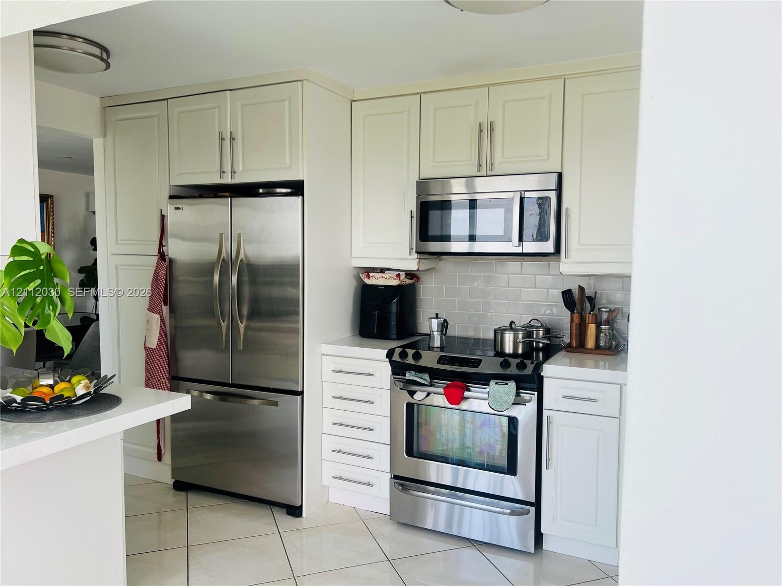 Kitchen featuring white cabinetry, stainless steel appliances, subway tile backsplash, white countertops, and tile flooring