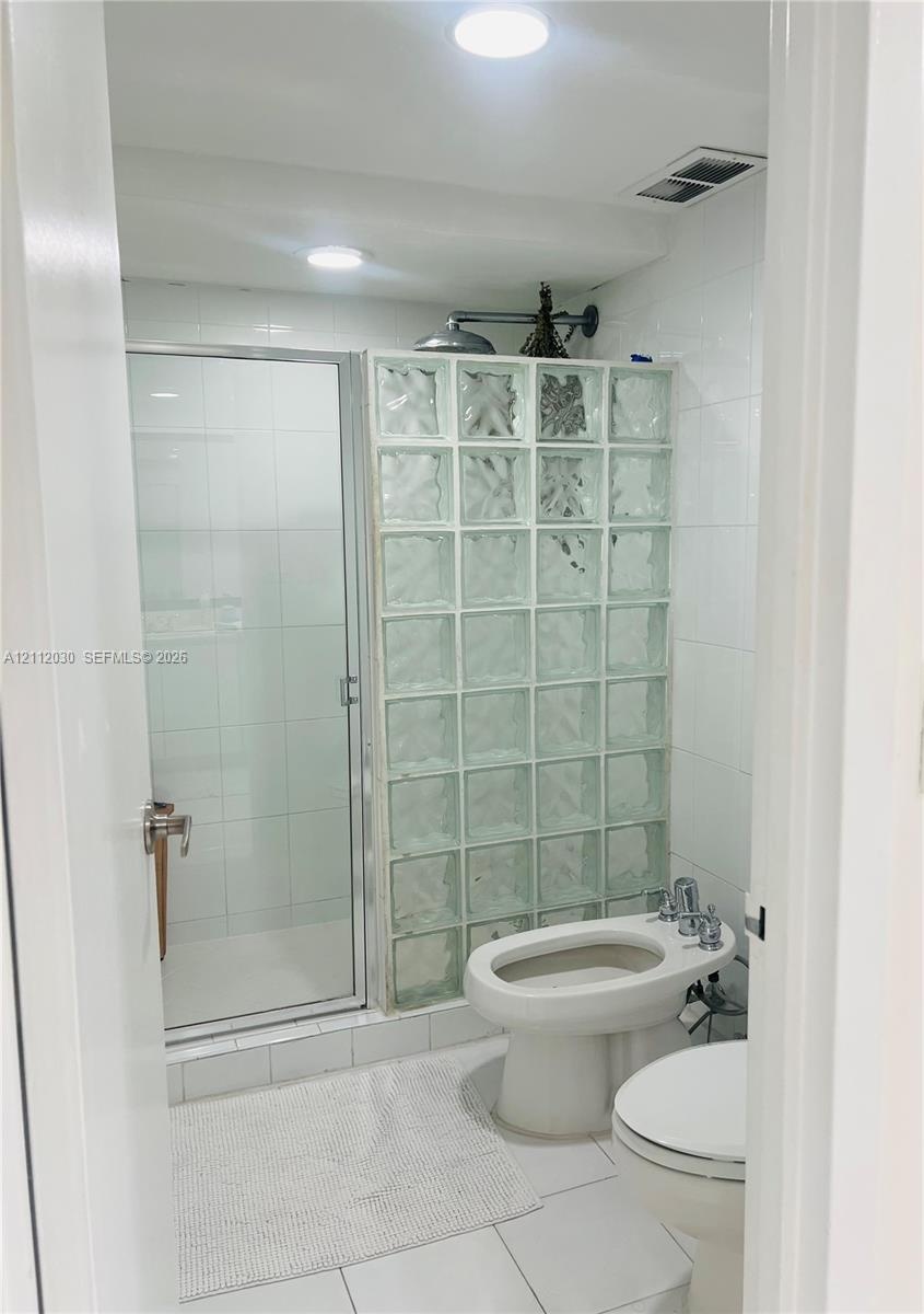 Glass block shower partition, walk-in shower with rainfall showerhead, ceramic tile walls, and bidet