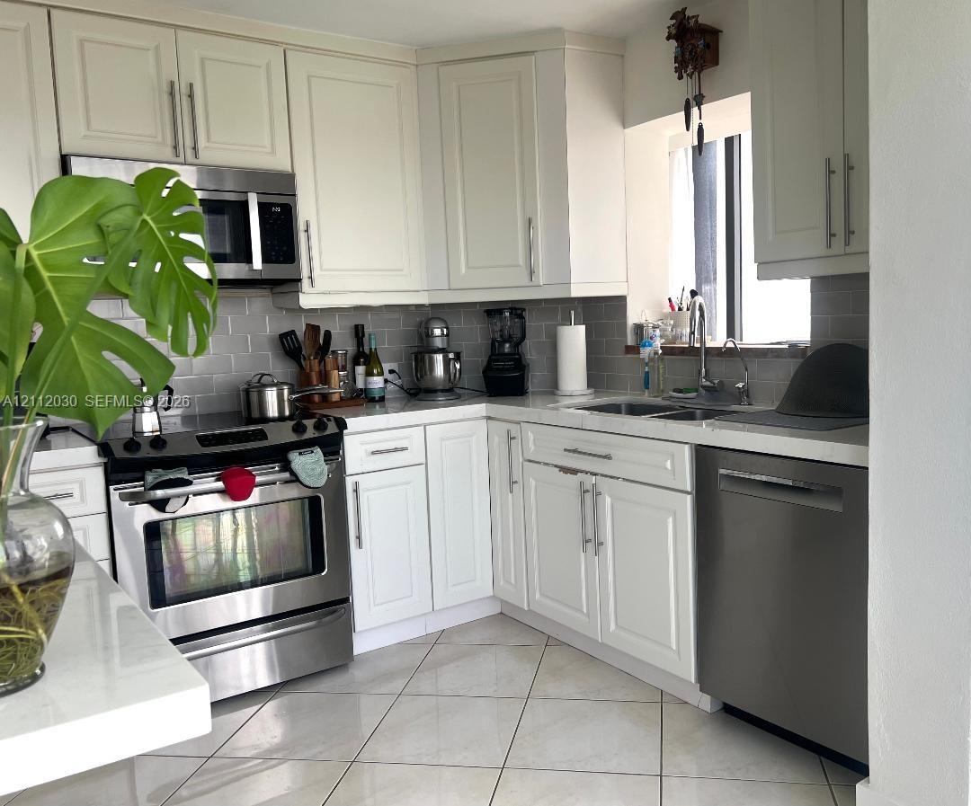 Kitchen featuring white shaker-style cabinetry, stainless steel appliances, subway tile backsplash, solid-surface countertops, and diagonal-set tile f