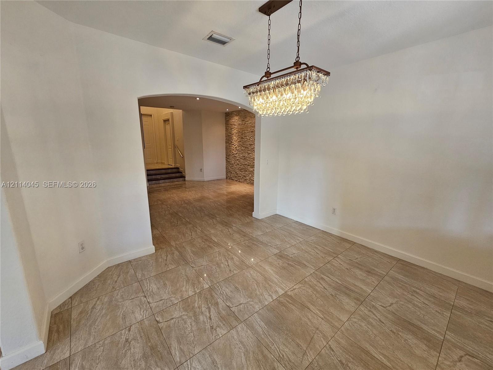 Large-format tile flooring, tiered crystal chandelier, arched entryway, and stone-accented wall finish
