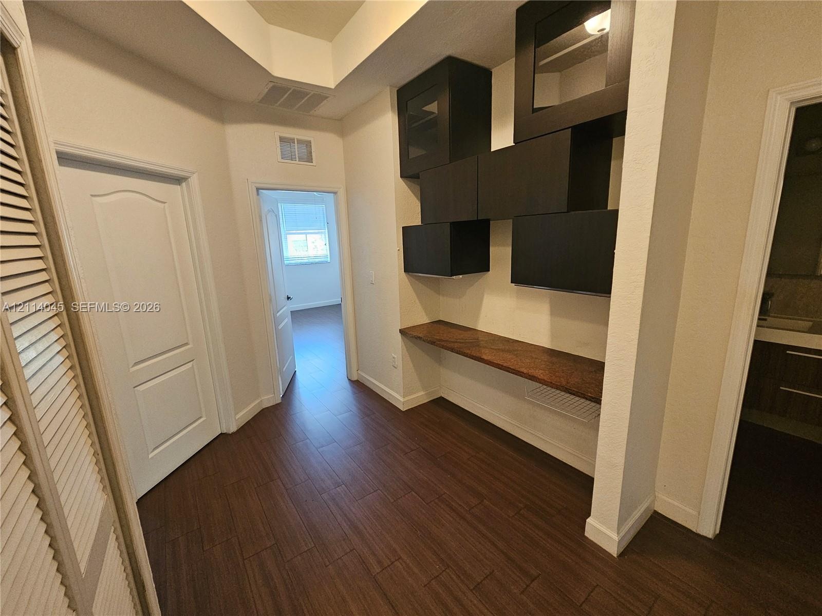 Built-in dark cabinetry with glass-front uppers, wood-finish flooring, and stone-surface desk area featuring recessed tray ceiling