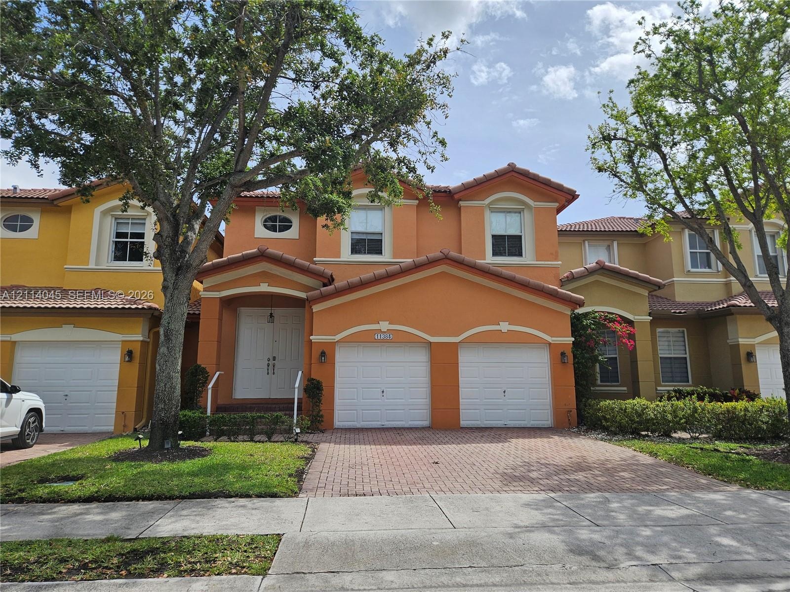 Two-story residence featuring a tile roof, stucco exterior, double-entry doors, and a paver driveway leading to a two-car garage
