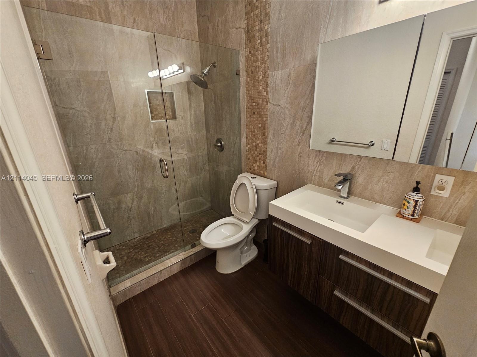 Walk-in shower with a glass enclosure, wall-mounted showerhead, and a recessed tiled niche, featuring a wood-finish floating vanity with a dual-basin 