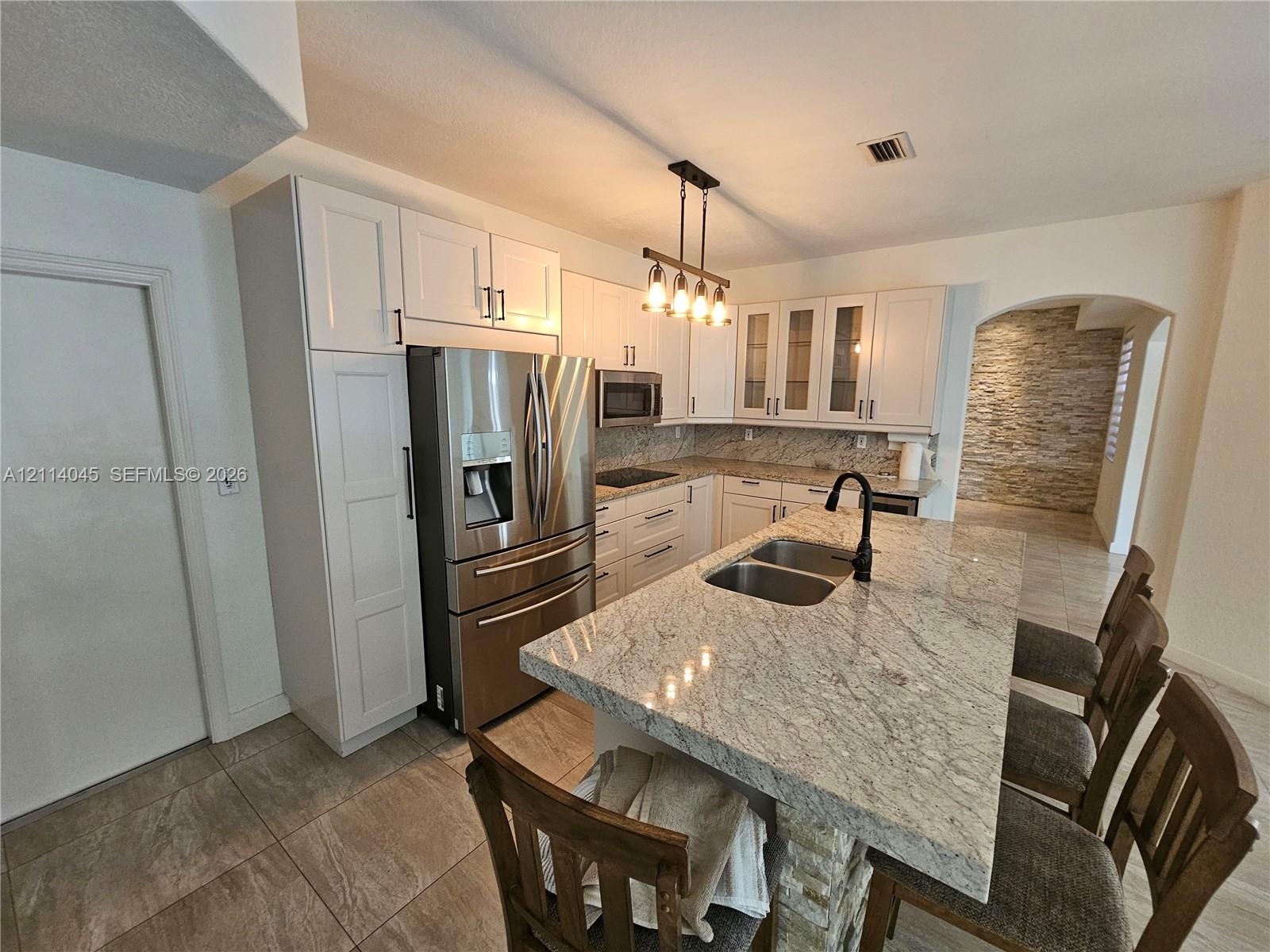 Kitchen featuring white cabinetry, stone-finish countertops, center island with a dual-basin undermount sink, stainless steel appliances, and tile flo