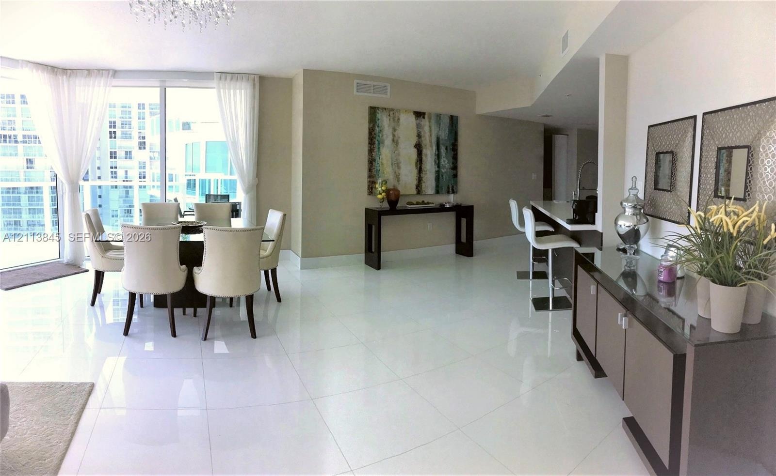 Open-concept living space featuring high-gloss tile flooring, floor-to-ceiling windows, and a built-in kitchen breakfast bar