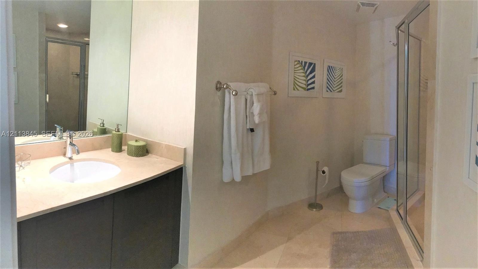 Bathroom featuring a vanity with a stone countertop, an integrated sink with a chrome faucet, full-width mirror, tile flooring, and a glass-enclosed s