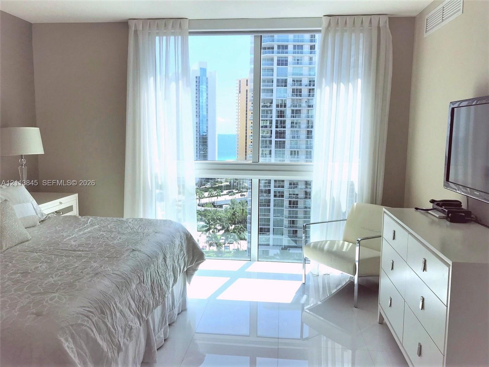 Floor-to-ceiling windows featuring urban and ocean scenery, high-gloss tile flooring, and neutral wall tones