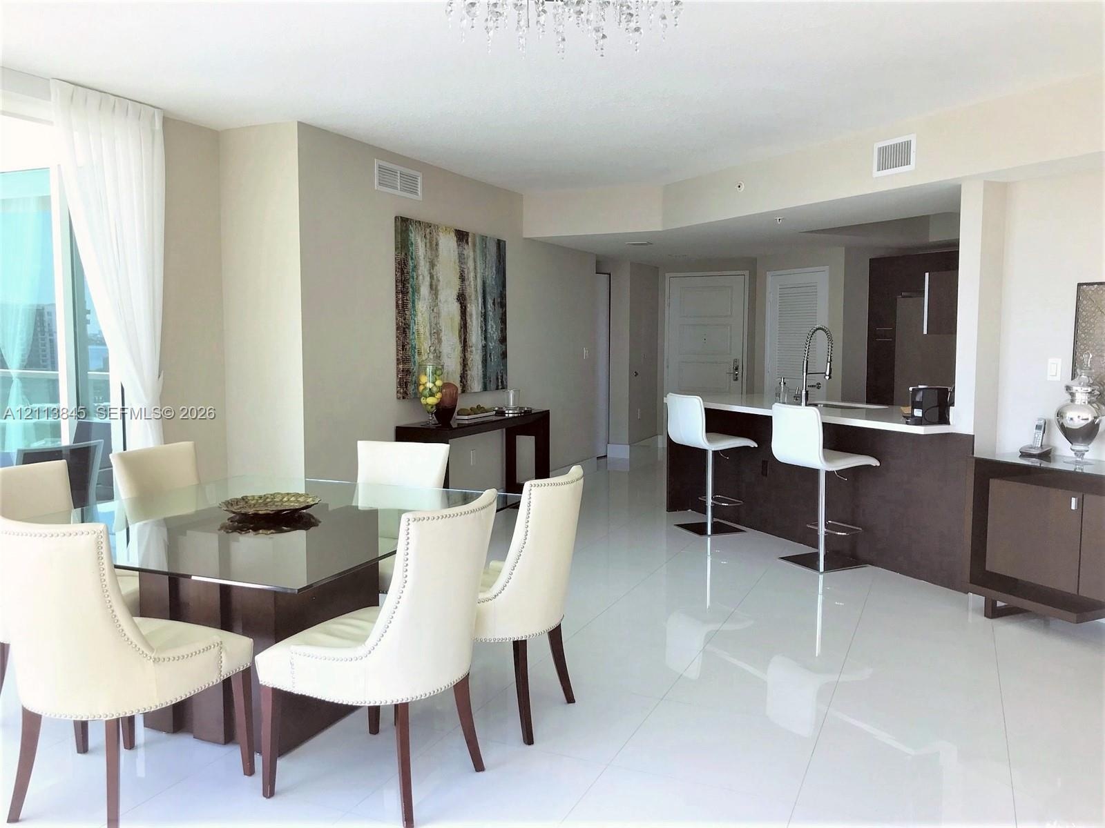 Open-concept living space featuring high-gloss tile flooring, crystal chandelier, kitchen with breakfast bar, dark-finish cabinetry, and floor-to-ceil