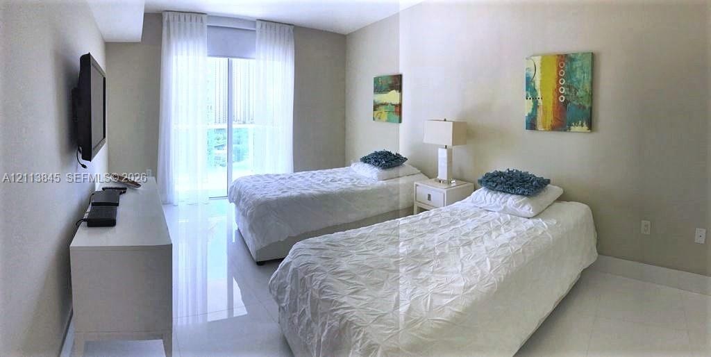 Neutral-toned walls, reflective tile flooring, and sliding glass door with balcony access