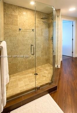 Walk-in shower featuring a frameless glass enclosure, neutral stone tile surround, integrated shower bench, square rainfall showerhead, and wood-finis