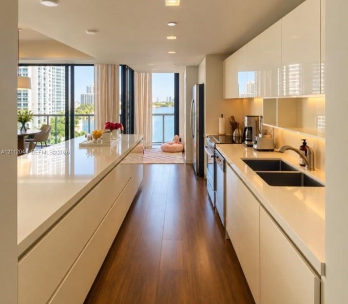 Modern kitchen featuring high-gloss cabinetry, expansive solid-surface countertops, wood-finish flooring, recessed lighting, and stainless steel appli