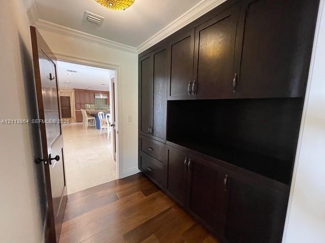 Dark wood built-in cabinetry featuring shaker-style doors, drawers, and open shelving, complemented by wood-finish flooring and crown molding