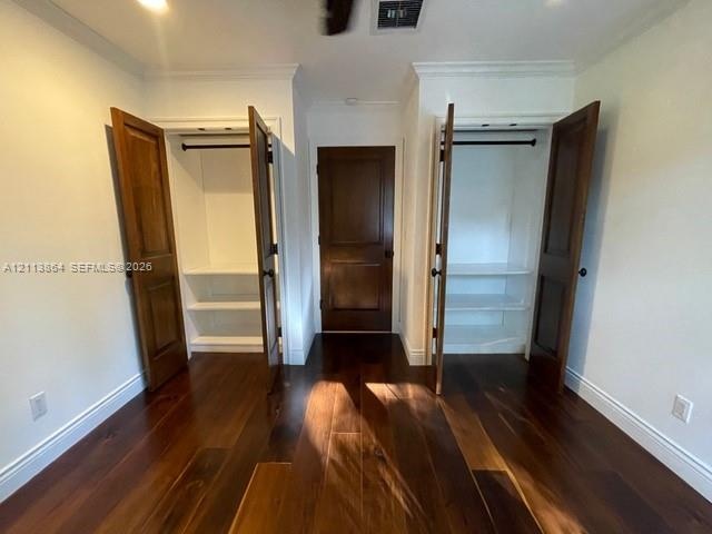 Room featuring dark-stained wood-finish flooring, two dual-door closets with built-in shelving, and a solid-core wood-finish swing door