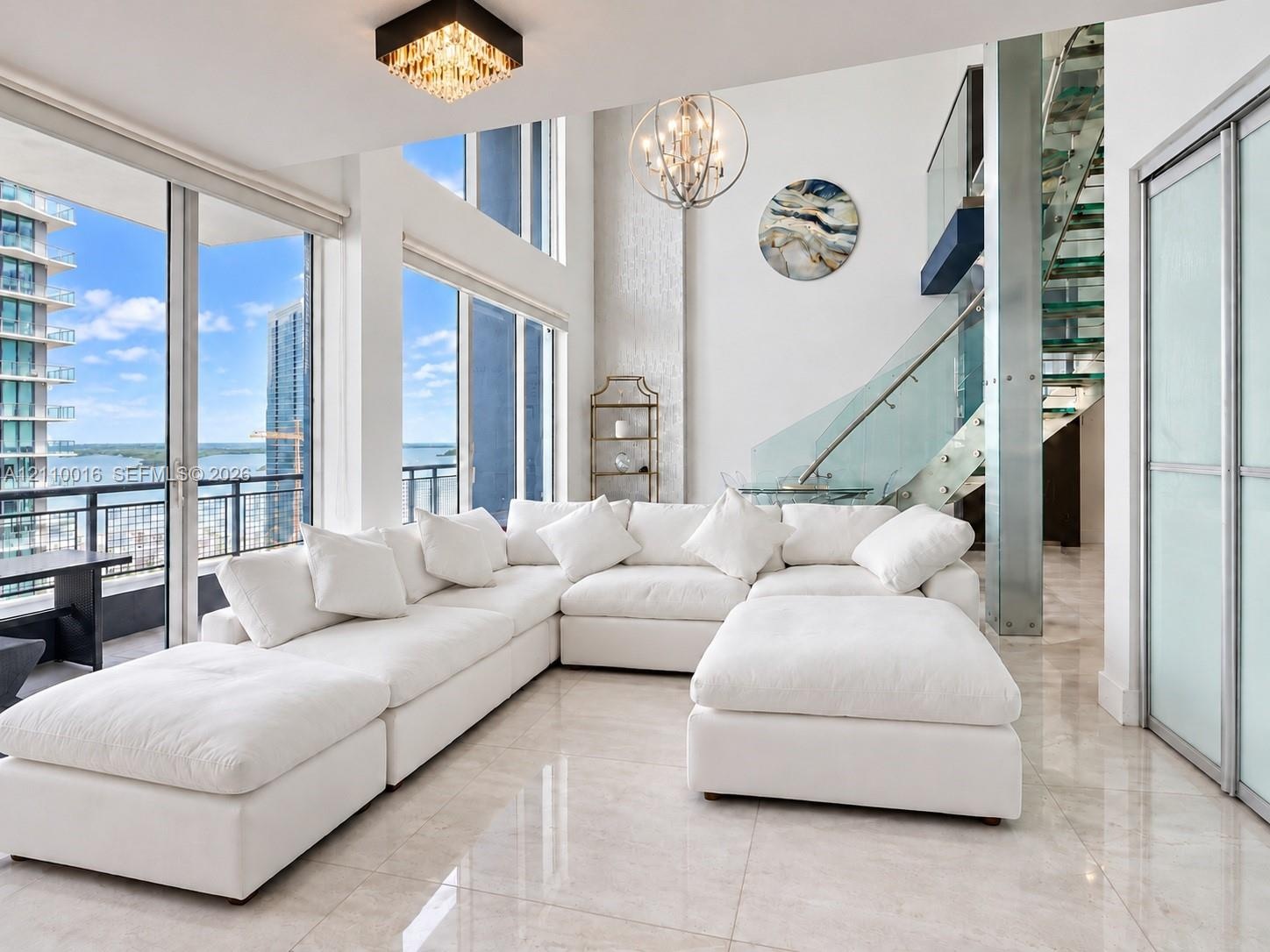 Kitchen featuring white cabinetry, stainless steel appliances, and large-format tile flooring, complemented by a curved staircase with glass treads an