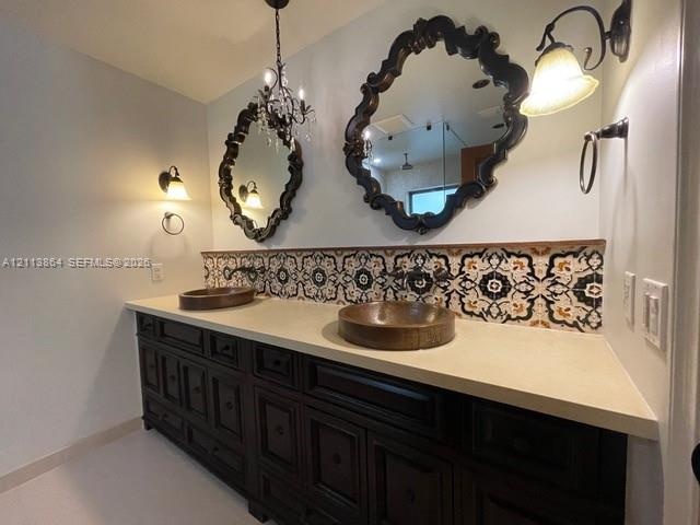 Double vanity featuring dark wood cabinetry, a solid surface countertop, dual vessel sinks, decorative patterned tile backsplash, and ornate wall-moun