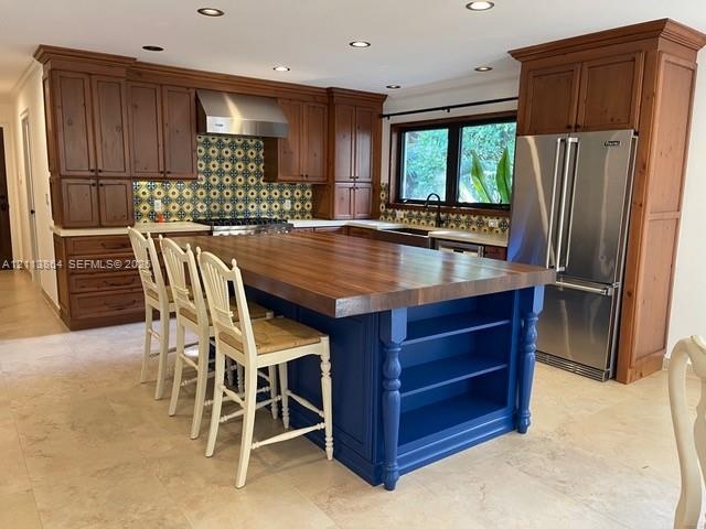 Kitchen featuring natural wood cabinetry, a central island with a wood countertop and open shelving, patterned tile backsplash, stainless steel applia
