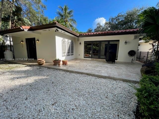 Exterior space featuring a neutral stucco finish, clay tile roof, expansive stone paver patio, multi-panel glass door systems, and decorative iron wal