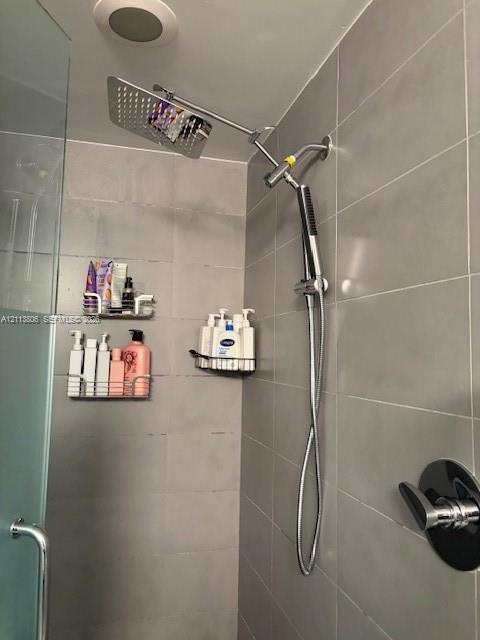 Walk-in shower featuring large-format grey tile wall cladding, an oversized square rainfall showerhead, a multi-function handheld shower wand, and a s