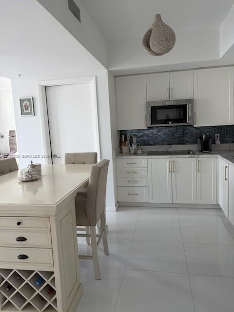 Kitchen featuring shaker-style cabinetry, stainless steel microwave, stone-finish countertops, tile backsplash, and built-in wine storage