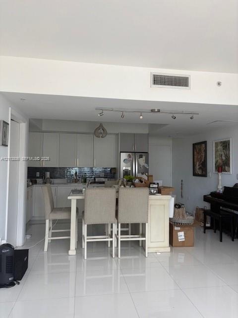 Kitchen featuring white cabinetry, a tiled backsplash, a central island, track lighting, and white tile flooring