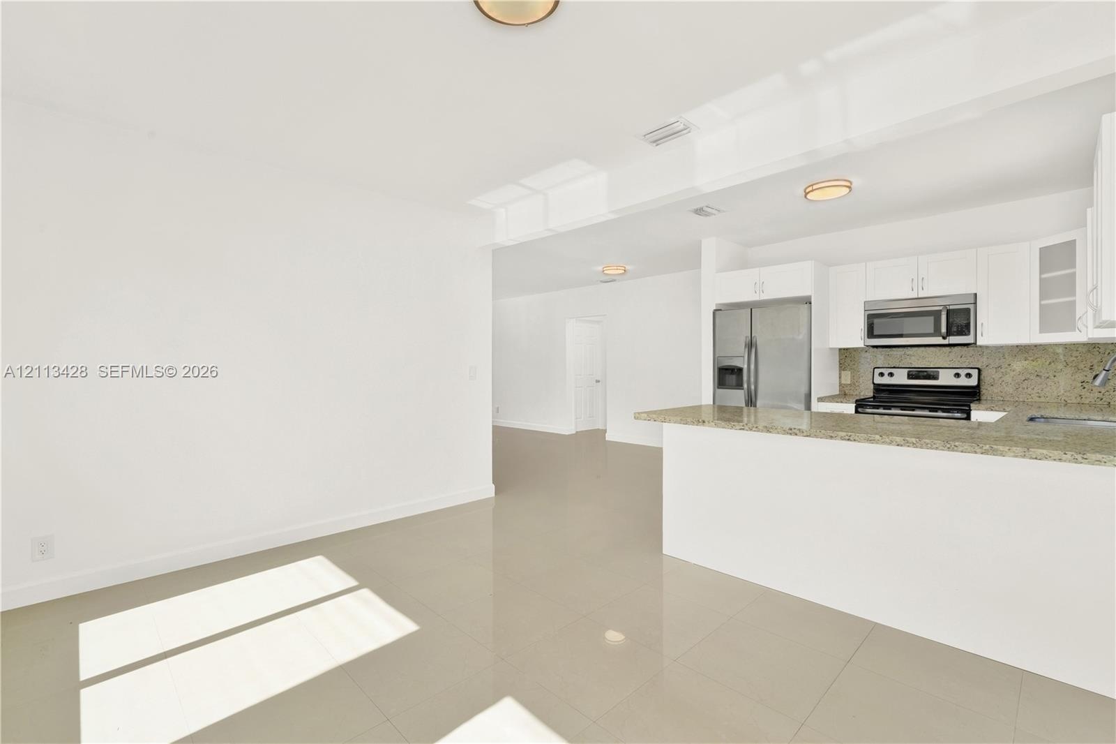 Kitchen featuring white cabinetry, stone-surface countertops, stone-finish backsplash, and stainless steel appliances, complemented by large-format ti