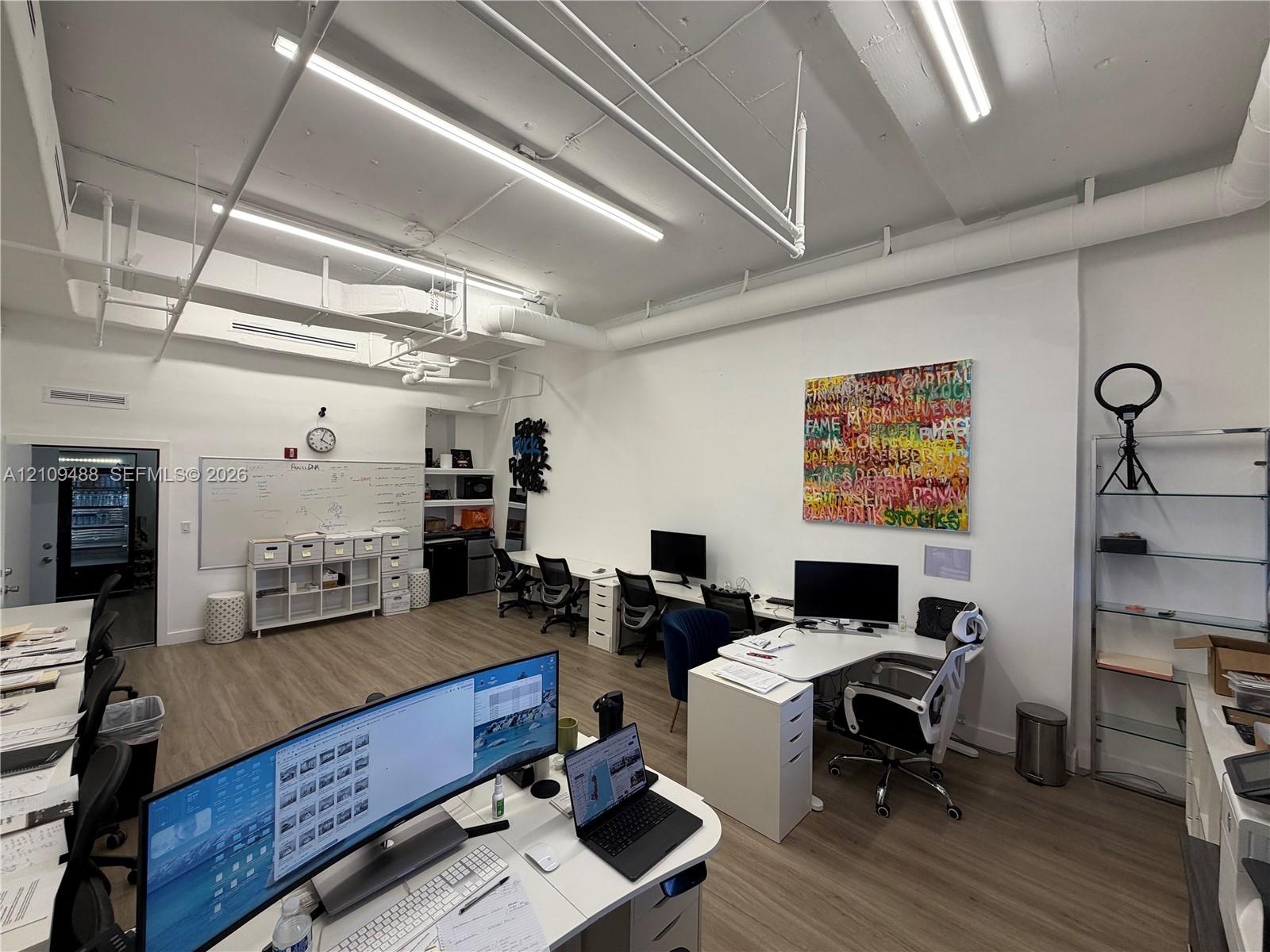 Open-concept workspace featuring wood-finish flooring, exposed industrial-style ductwork, and high-output linear lighting fixtures