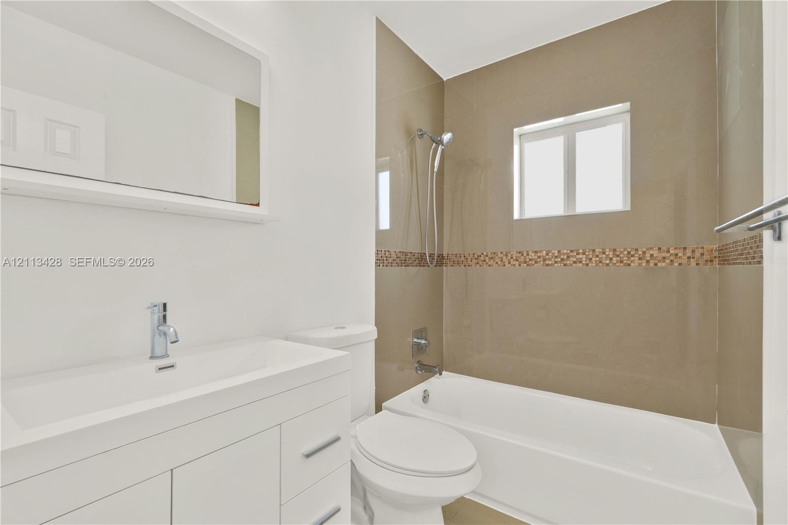 Bathroom featuring a white vanity with an integrated basin, a large wall-mounted mirror, a bathtub with a tiled shower surround, and a chrome hand-hel