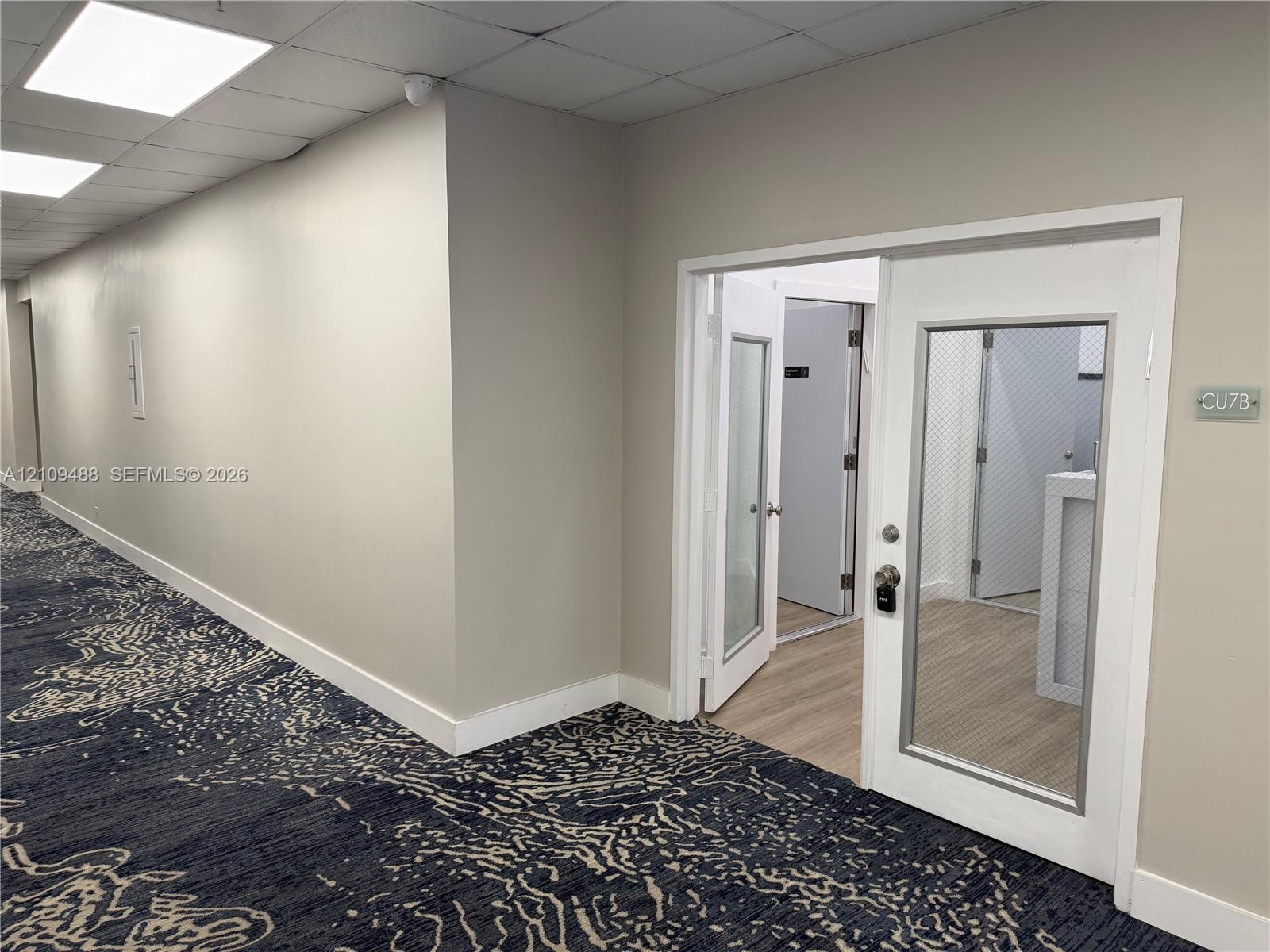 Entryway featuring a single door with a glass inlay, neutral wall paint, wood-finish flooring, and drop ceiling panels with recessed lighting