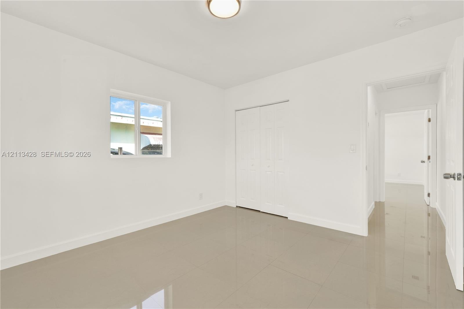 Neutral-toned tile flooring, white interior walls, sliding door closet, single-pane window, and flush-mount ceiling lighting