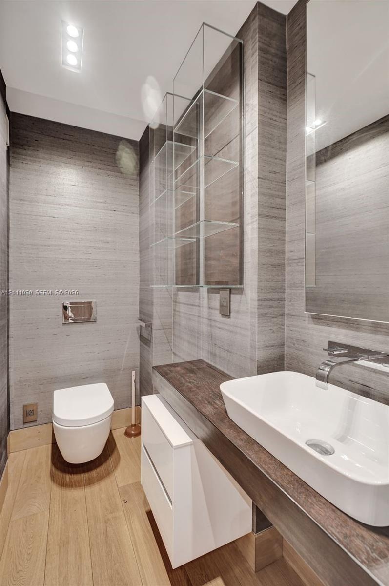 Wall-mounted toilet with recessed flush plate, vessel sink with wall-mounted polished chrome faucet, custom wood-finish vanity countertop, integrated 