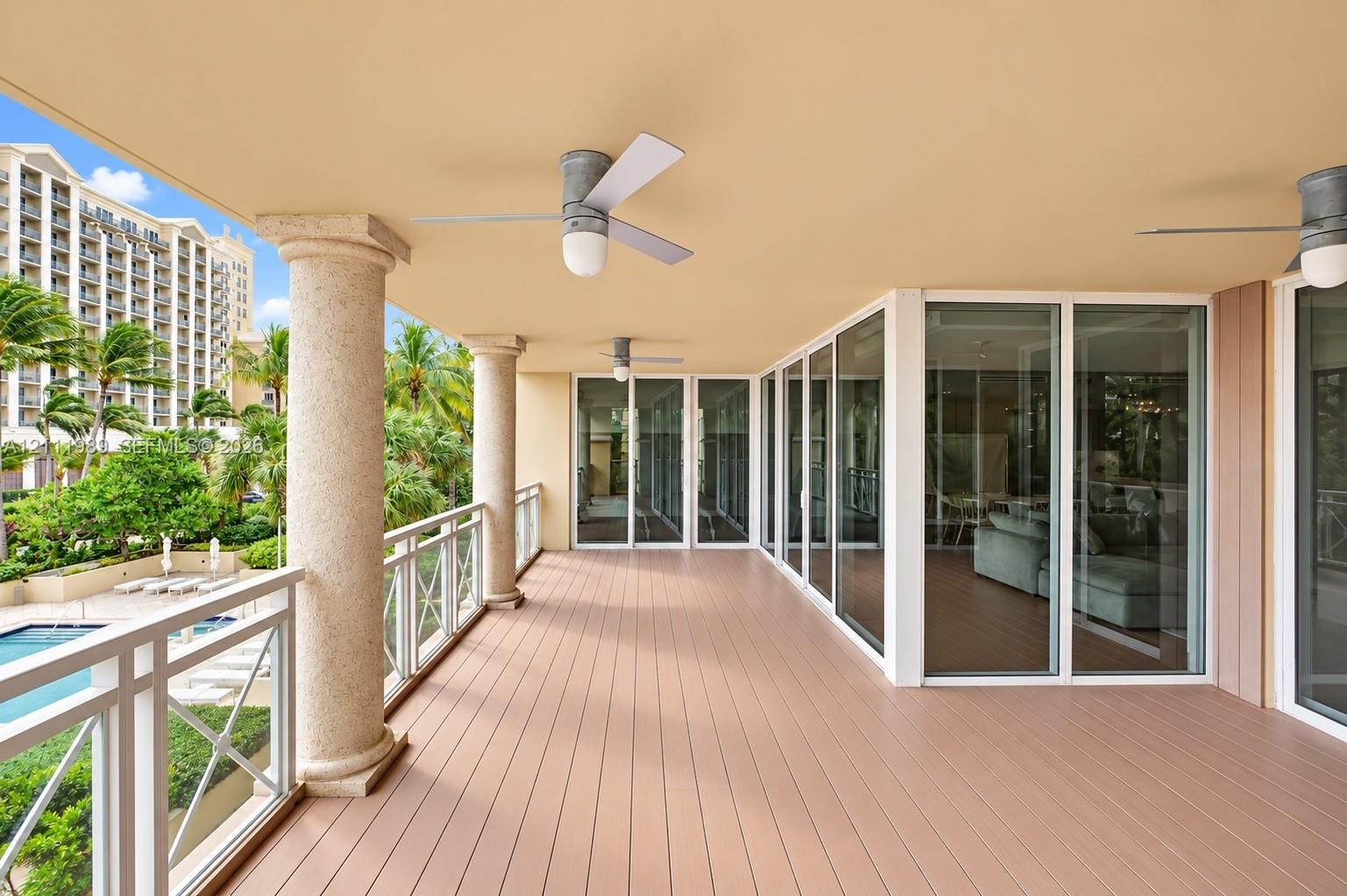 Covered terrace featuring composite decking, structural columns, ceiling-mounted fans, and sliding glass wall panels