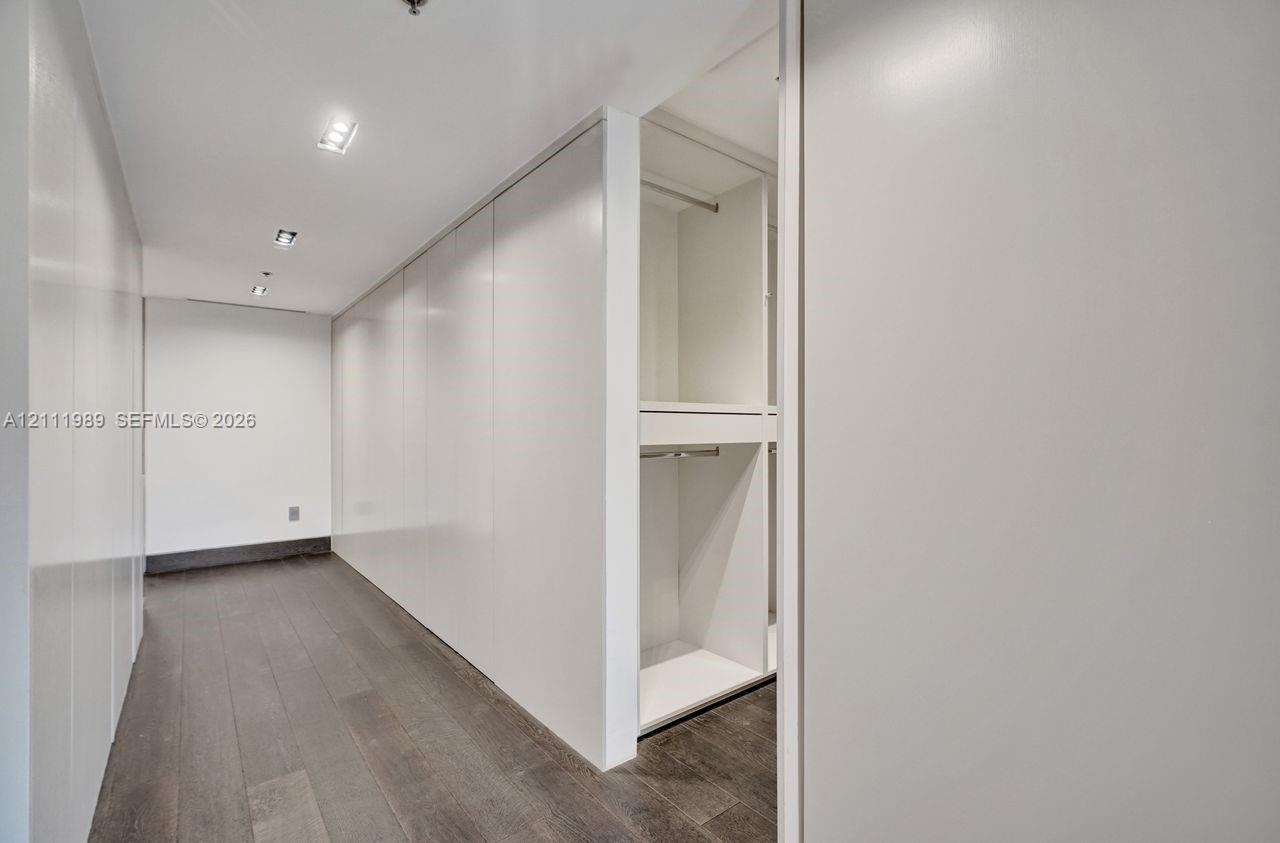 Floor-to-ceiling built-in cabinetry with a smooth white finish, integrated closet shelving, recessed ceiling lighting, and dark wood-finish flooring