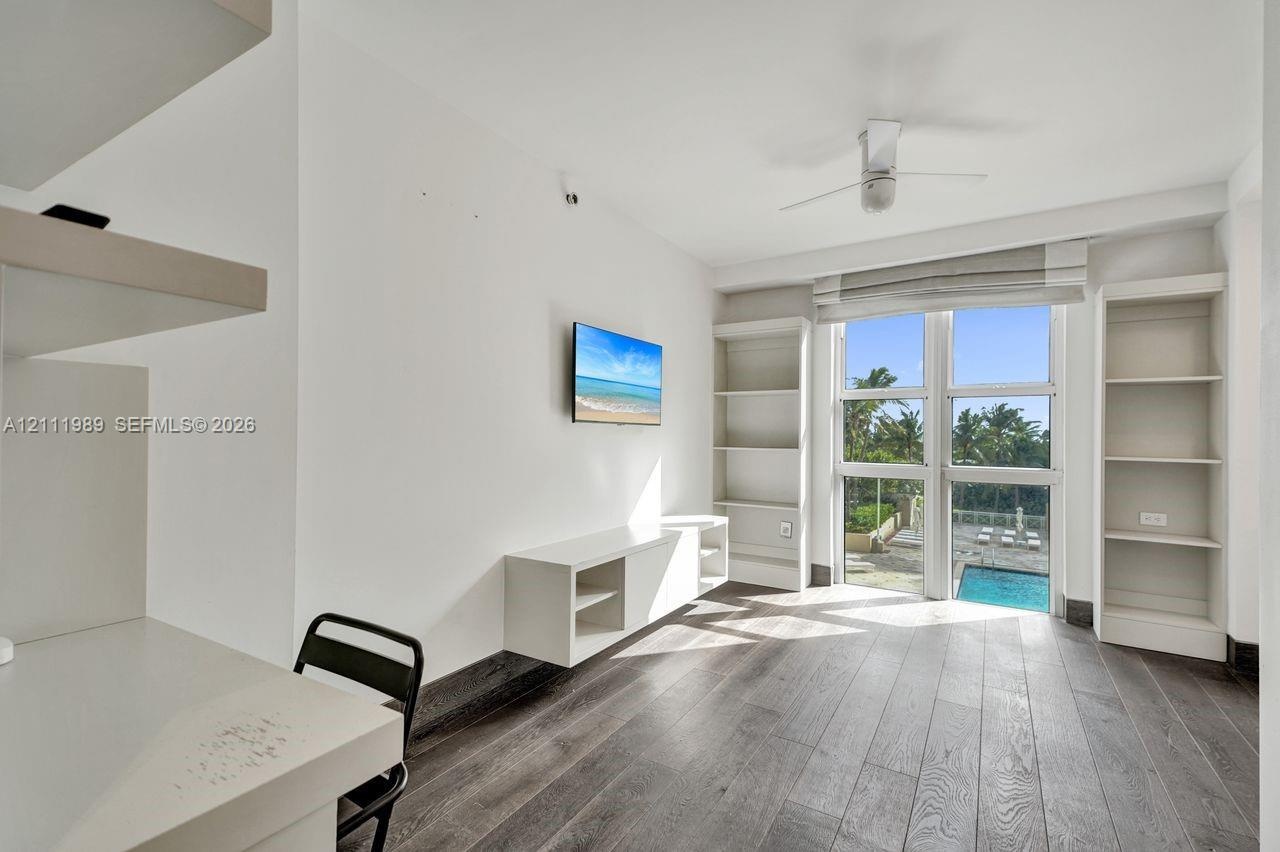 Wood-finish flooring, floor-to-ceiling windows, built-in shelving, white media console, and ceiling fan