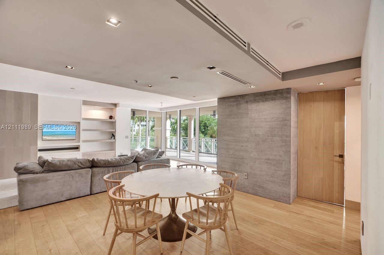Open-concept area featuring wood-finish flooring, recessed lighting, built-in shelving, a textured stone-finish accent wall, and floor-to-ceiling glas