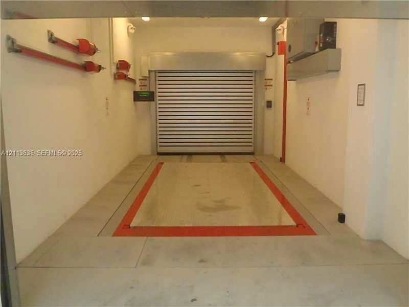 Automated vehicle elevator featuring a metal platform, industrial rolling steel door, surface-mounted wall tracks, and recessed ceiling lighting