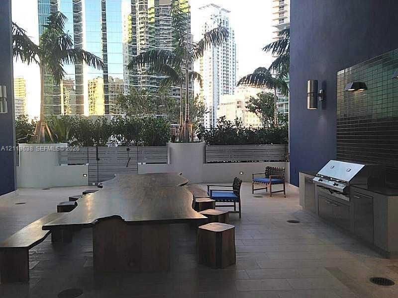 Outdoor terrace featuring a built-in stainless steel grill, dark-toned tile backsplash, stone-finish flooring, integrated wall-mounted lighting, and c