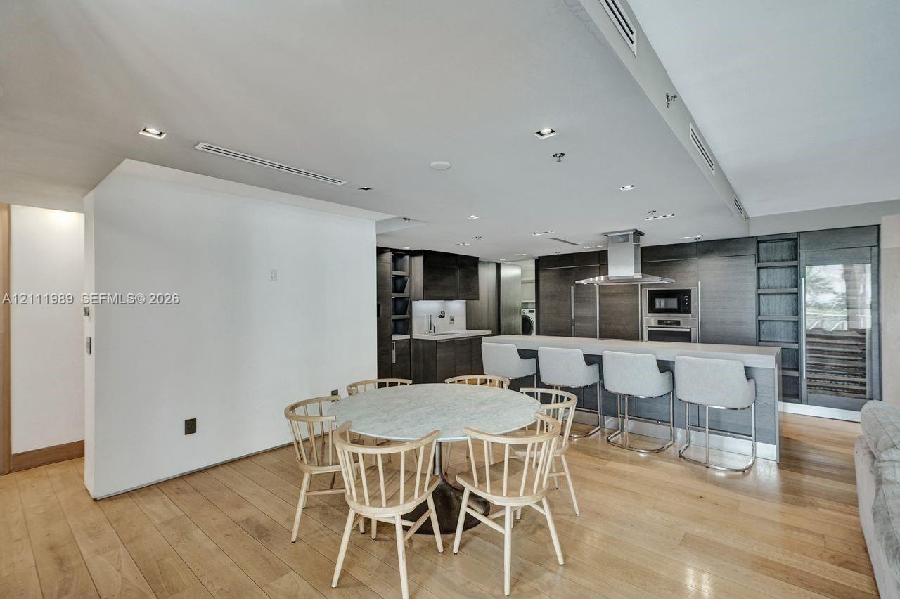 Contemporary kitchen featuring custom cabinetry, integrated stainless steel appliances, a large stone-topped island with seating, recessed ceiling lig