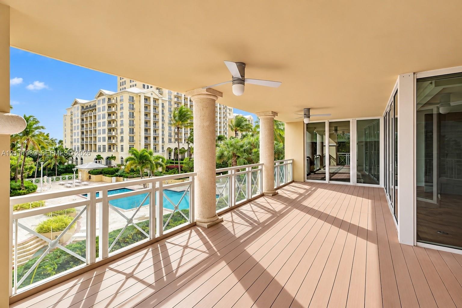 Covered balcony featuring wood-finish flooring, structural columns, white cross-pattern railings, and ceiling-mounted fans