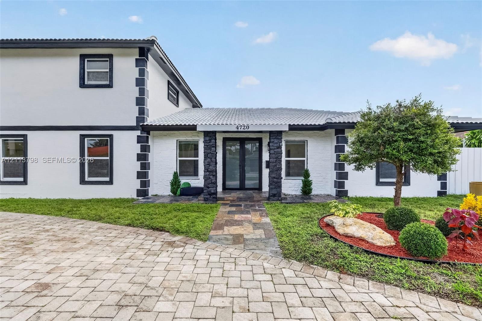 Two-story exterior featuring a white-painted brick facade with dark contrast trim, stone-clad porch columns, a multi-colored stone paver walkway, and 