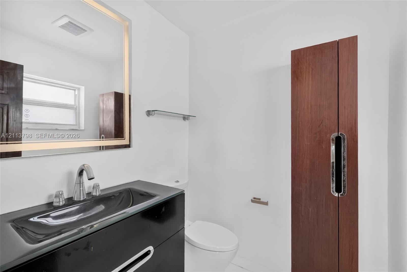 Modern vanity with an integrated sink, backlit rectangular mirror, sleek wood-finish cabinetry, and contemporary polished-chrome fixtures