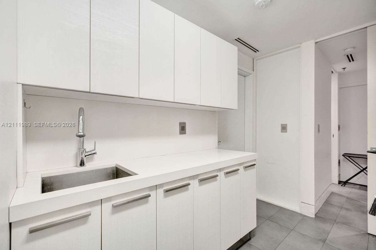 Custom white cabinetry, solid surface countertop, stainless steel undermount sink, high-arc chrome faucet, and tile flooring