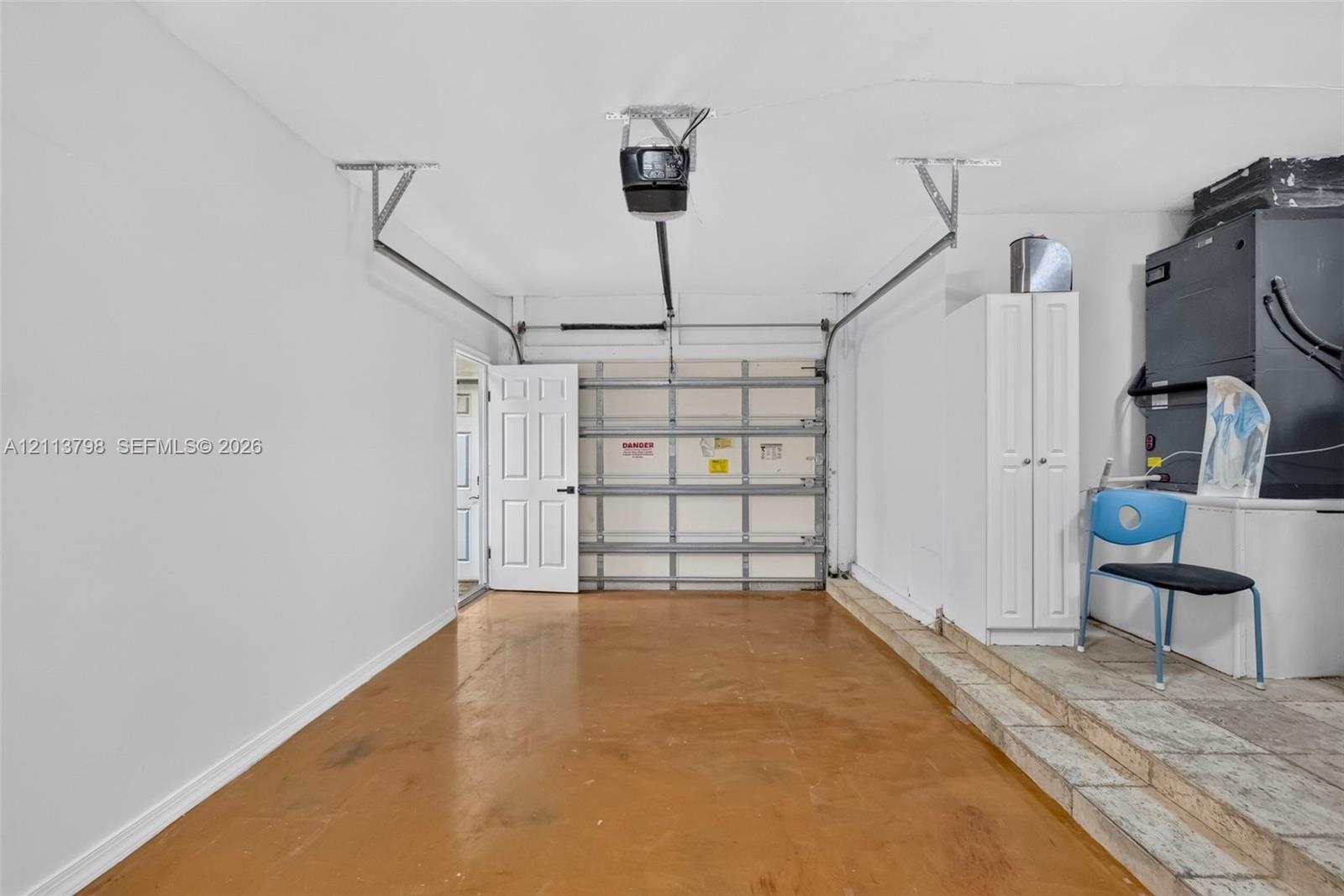 Single-car garage featuring a roll-up door, automated door opener, built-in storage cabinetry, and concrete flooring