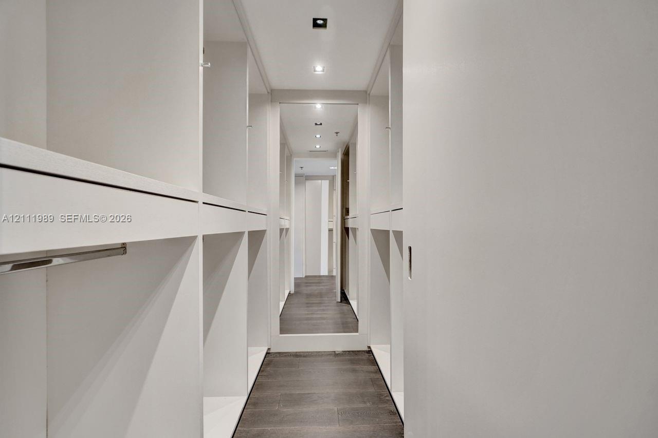 Custom floor-to-ceiling cabinetry, dark wood-finish flooring, full-length mirror, and recessed ceiling lighting