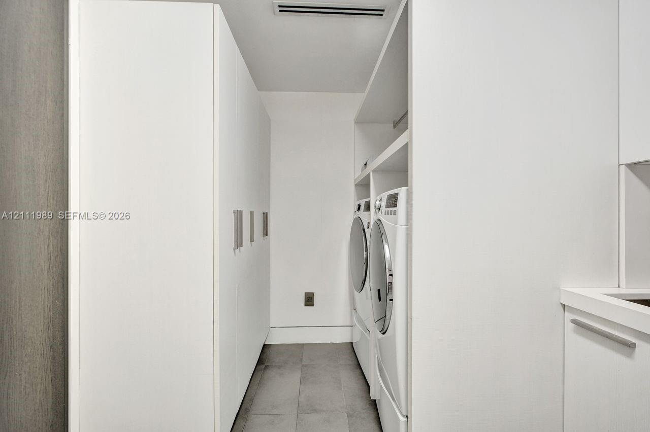 Laundry space featuring floor-to-ceiling white cabinetry, expansive open shelving, stone-finish tile flooring, and integrated white appliances